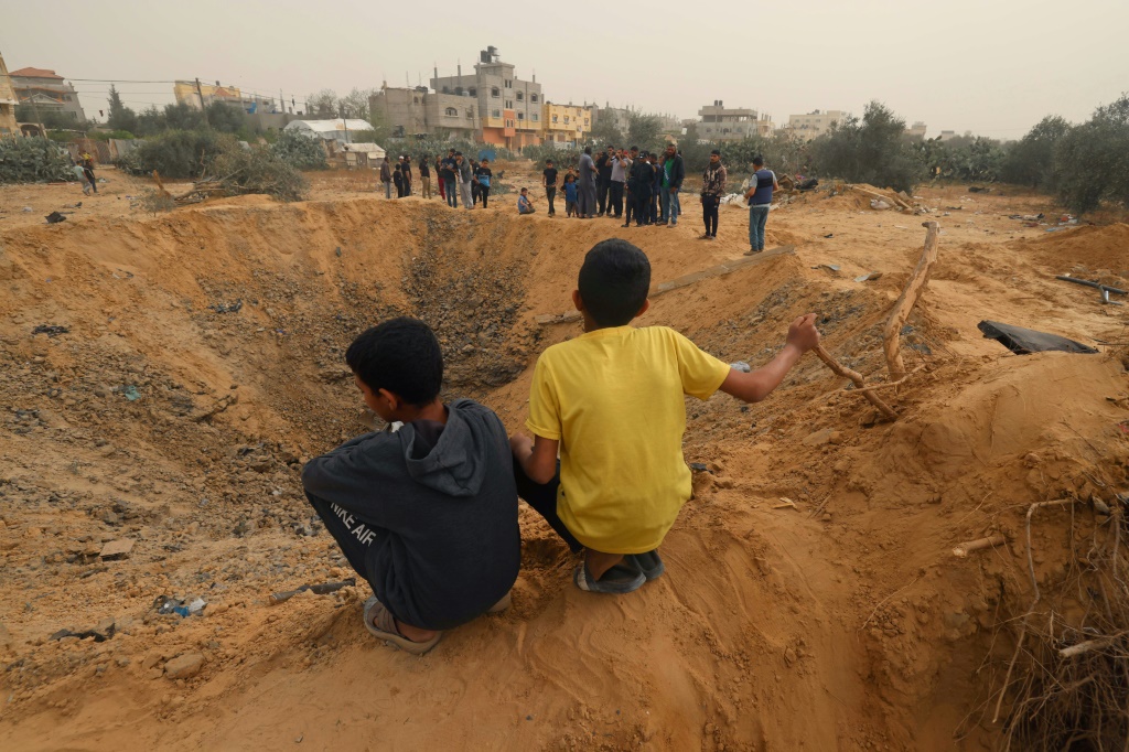    طفلان فلسطينيان ينظران إلى حفرة ضخمة خلّفها قصف إسرائيلي في رفح جنوبي قطاع غزة في 18 نيسان/أبريل 2024. (أ ف ب)   